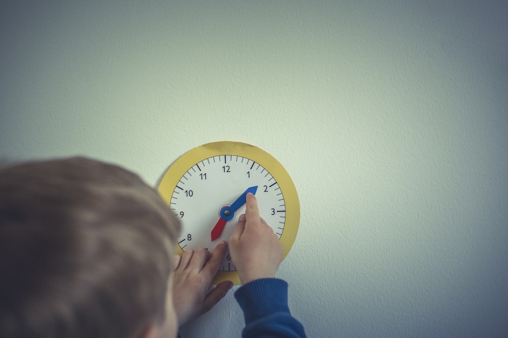 Persona en camisa azul de manga larga sosteniendo reloj de pared analógico redondo blanco