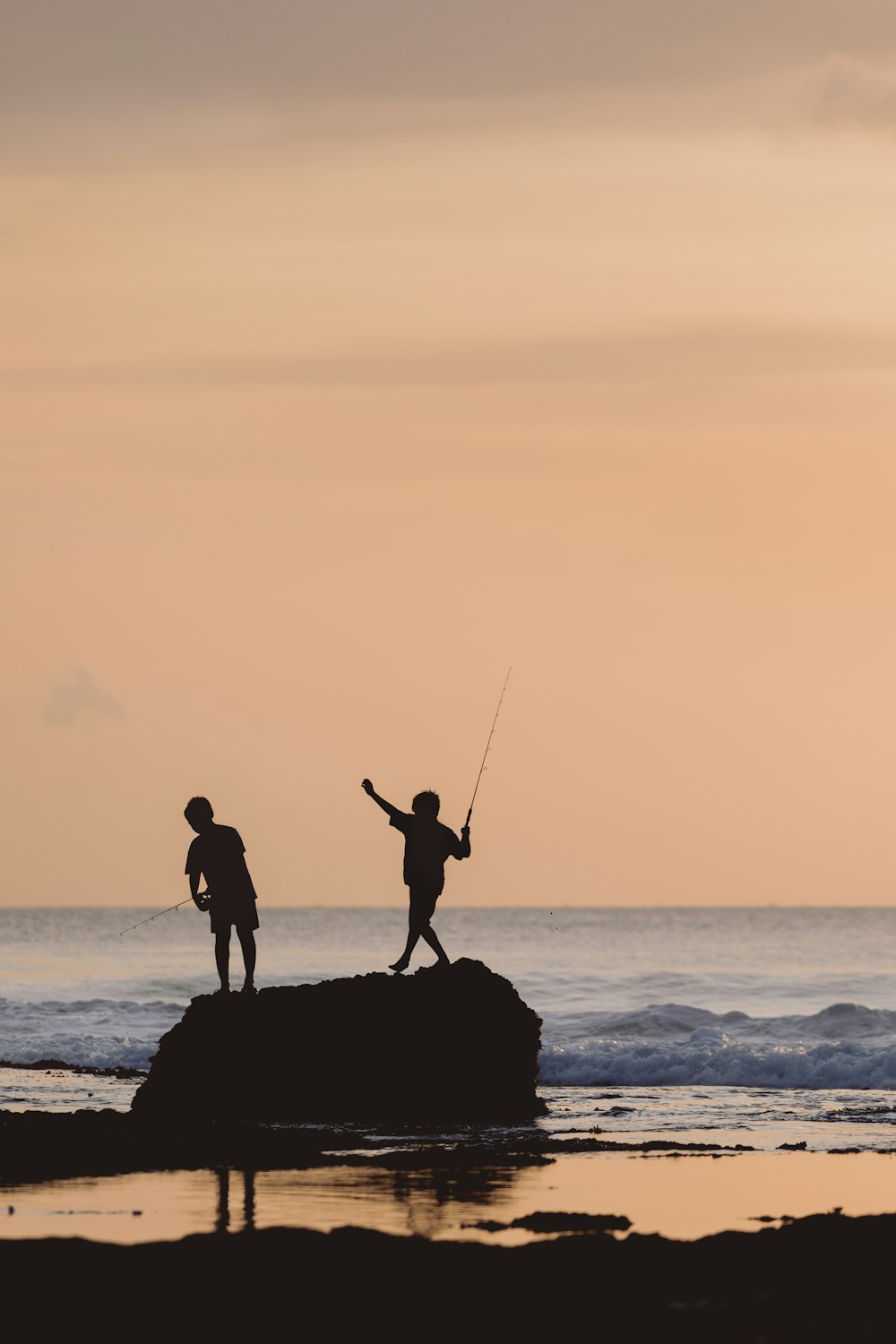 Silhouette von 2 Männern, die bei Sonnenuntergang am Strand angeln