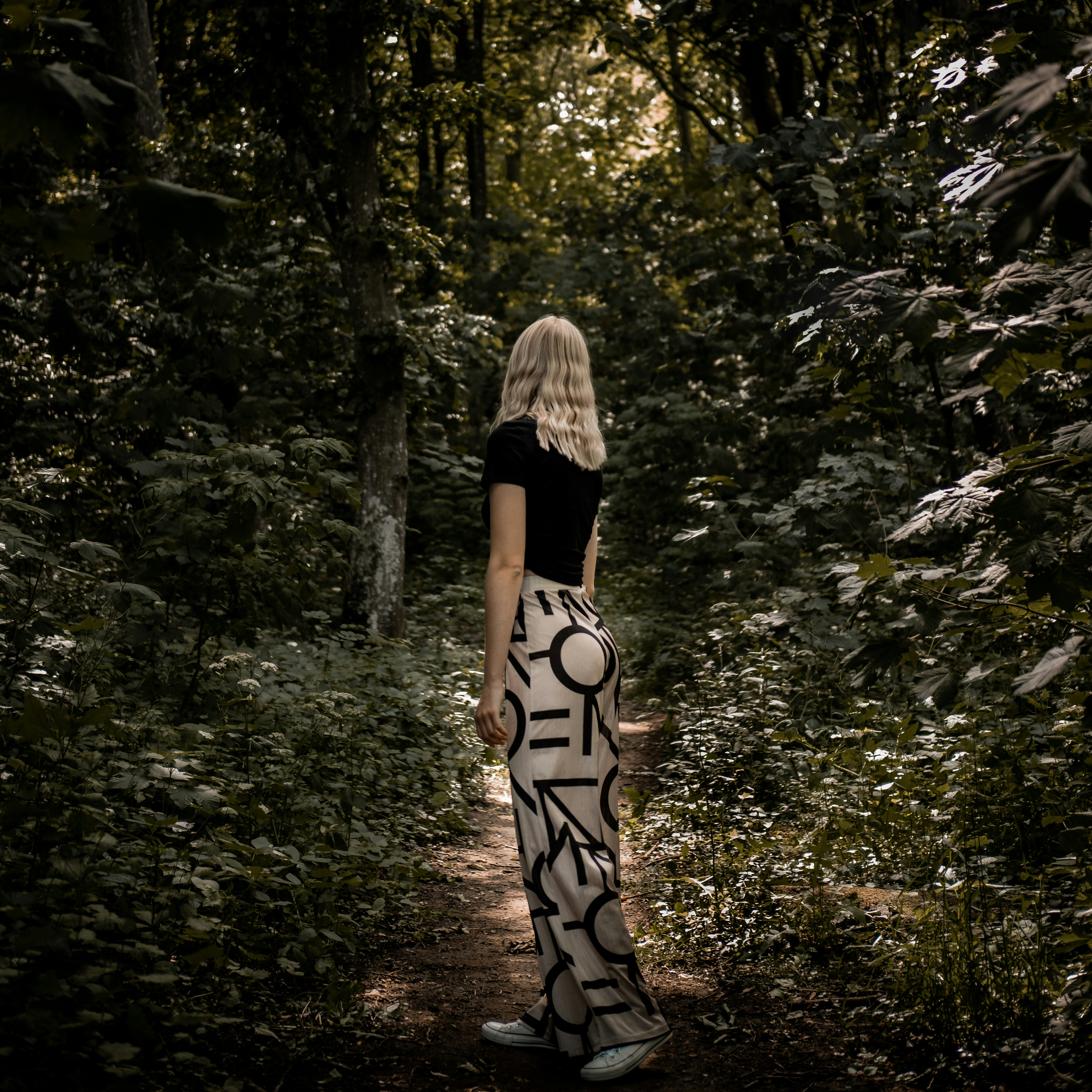 mulher no vestido preto e branco em pé no meio da floresta durante o dia