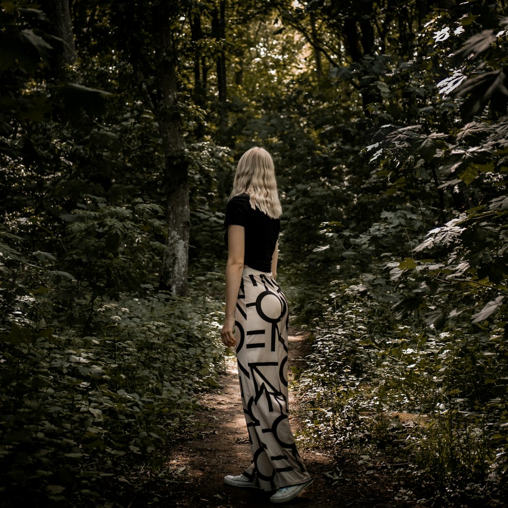 woman in black and white dress standing in the middle of the forest during daytime