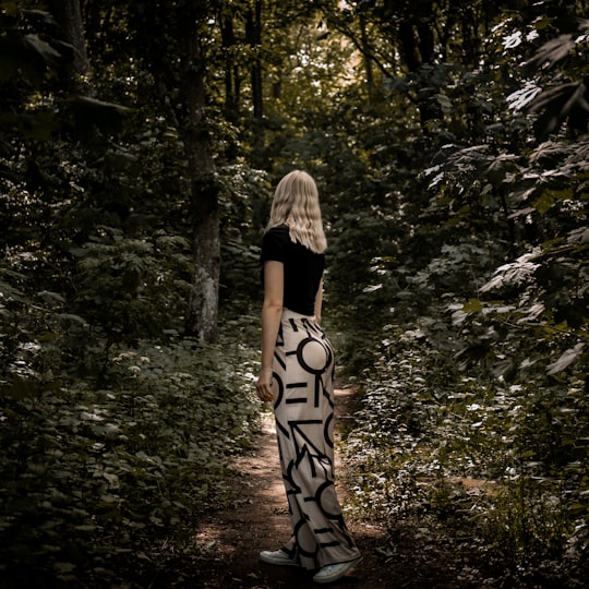 woman in black and white dress standing in the middle of the forest during daytime in Vä Sweden