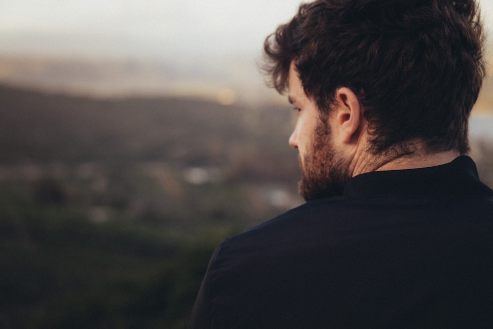 man in black shirt looking at the green grass field during daytime