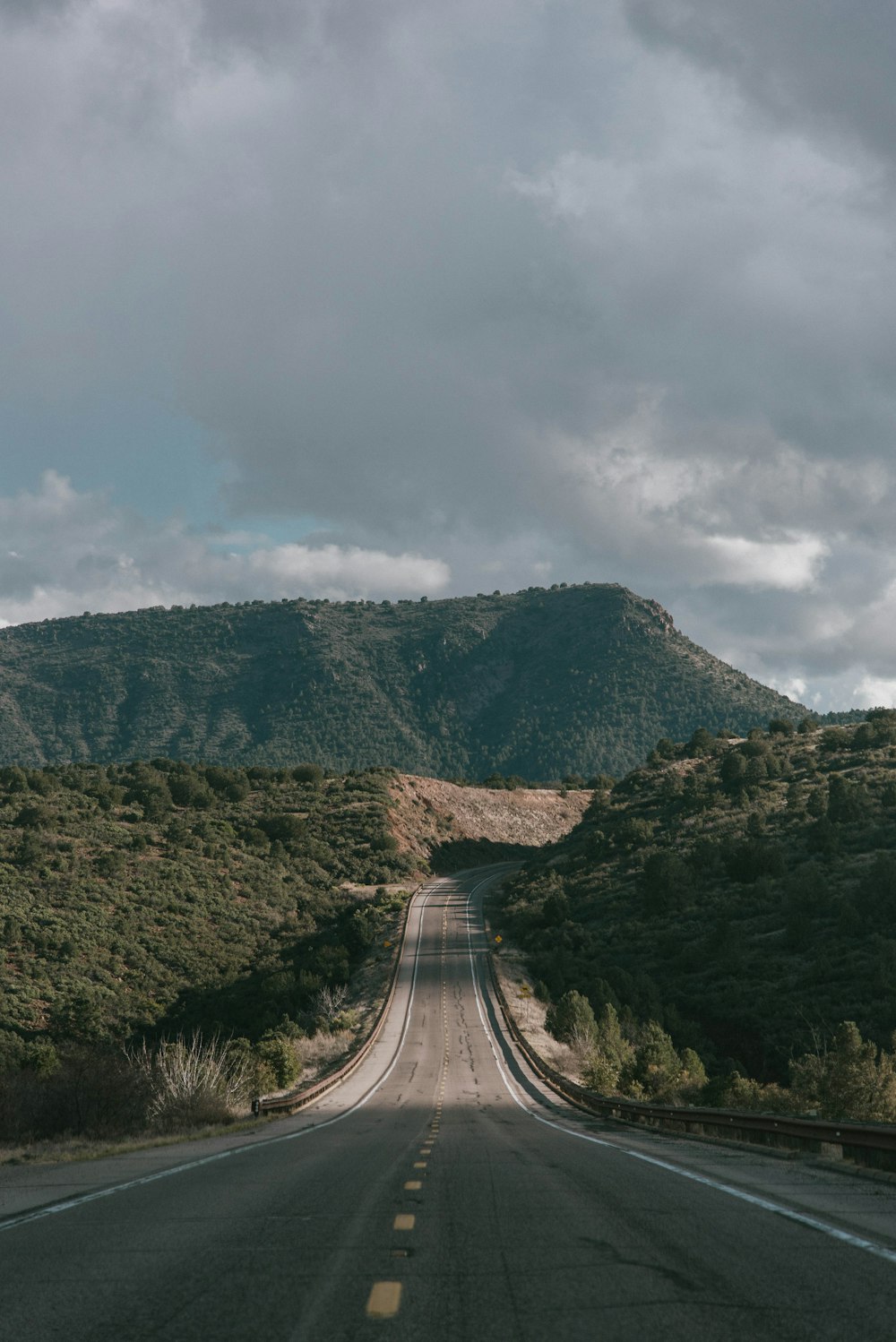 Carretera de hormigón gris entre montañas verdes bajo un cielo gris