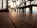 A beautifully stained wooden deck glowing warmly in the afternoon sun, surrounded by green plants.