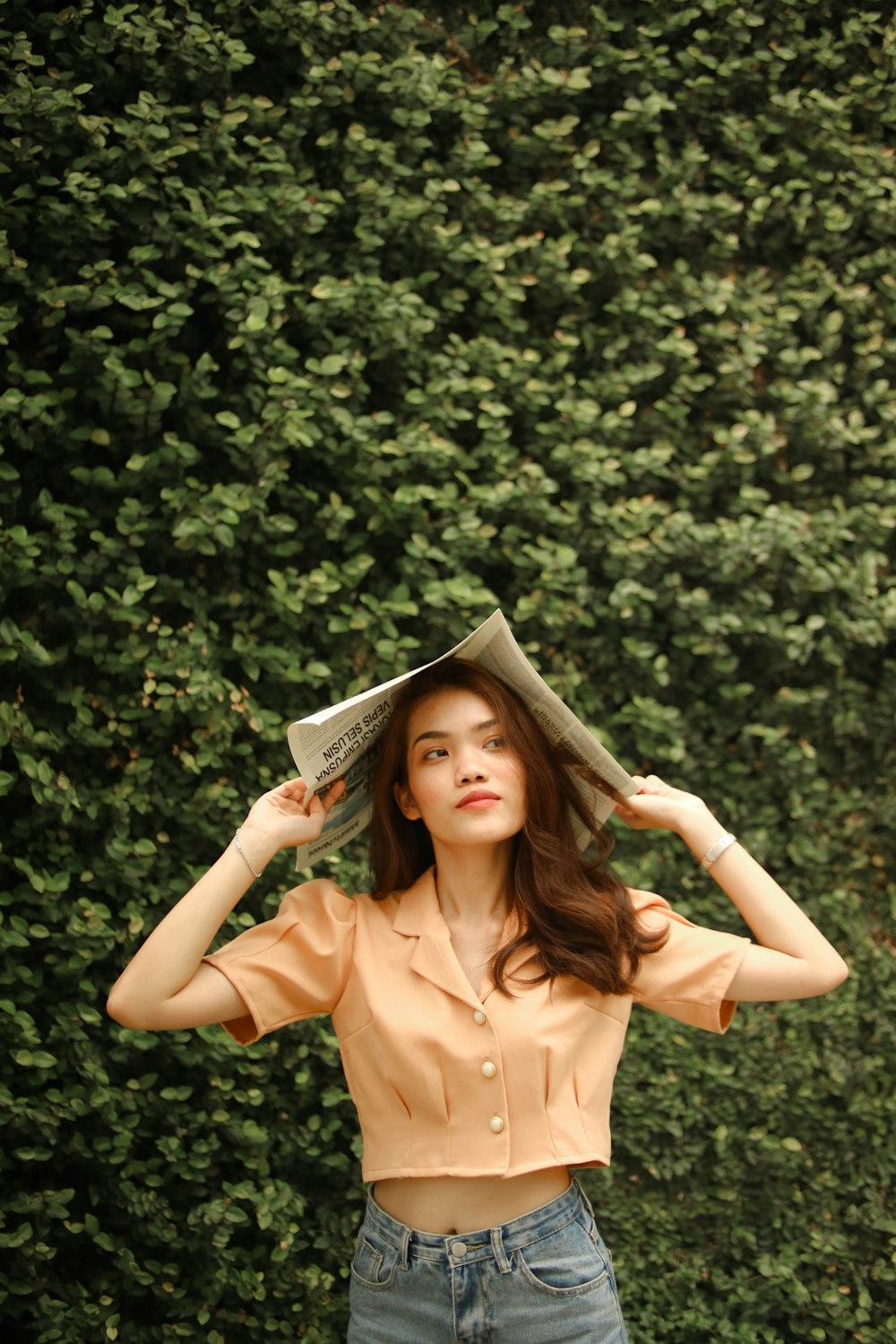 a woman standing in front of a bush with a hat on her head