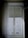A window with sheer curtains partially covering a view of an exterior building, featuring architectural details and multiple windows. A chandelier hangs at the upper right corner, adding a touch of elegance.