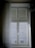 A window with sheer curtains partially covering a view of an exterior building, featuring architectural details and multiple windows. A chandelier hangs at the upper right corner, adding a touch of elegance.