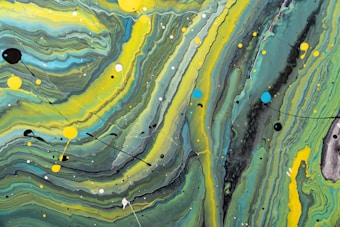 An abstract artwork featuring fluid, swirling patterns in shades of green, yellow, blue, and black. The composition includes various circular splatters and drips of paint, creating a dynamic and energetic visual effect.