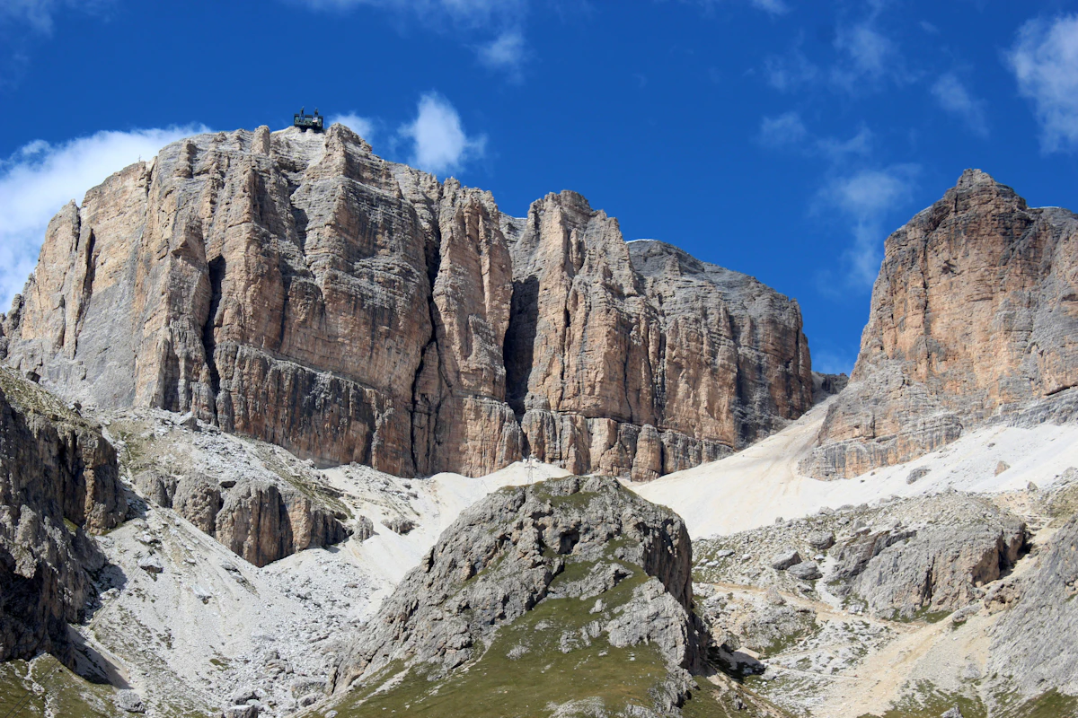 The rock walls of Sass Pordoi under a blue sky, with a building on the rim