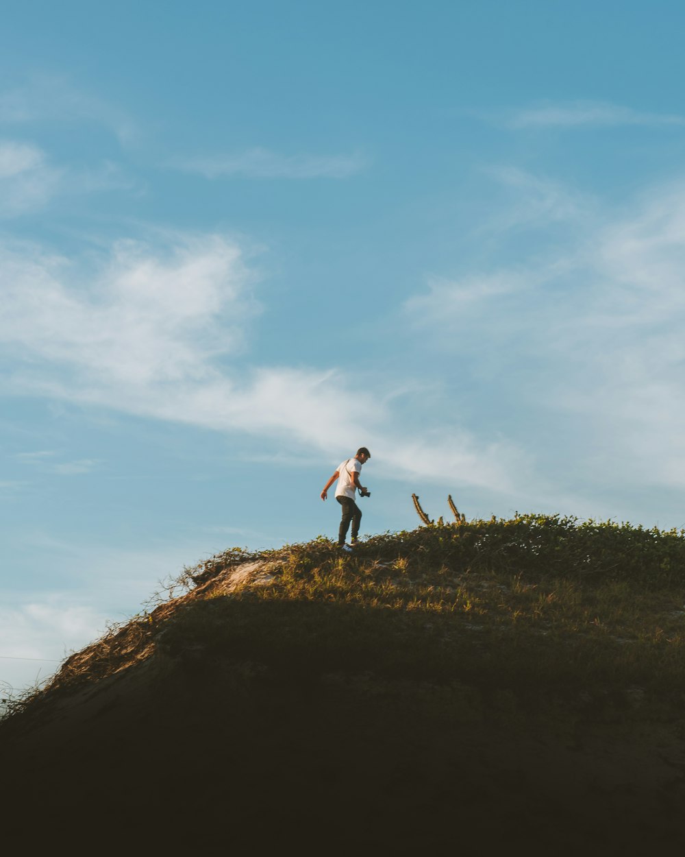 woman in white shirt and black pants standing on brown grass field under white clouds and