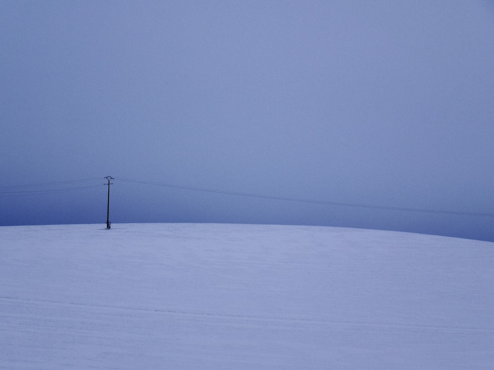schwarzer Strommast auf schneebedecktem Boden unter grauem Himmel
