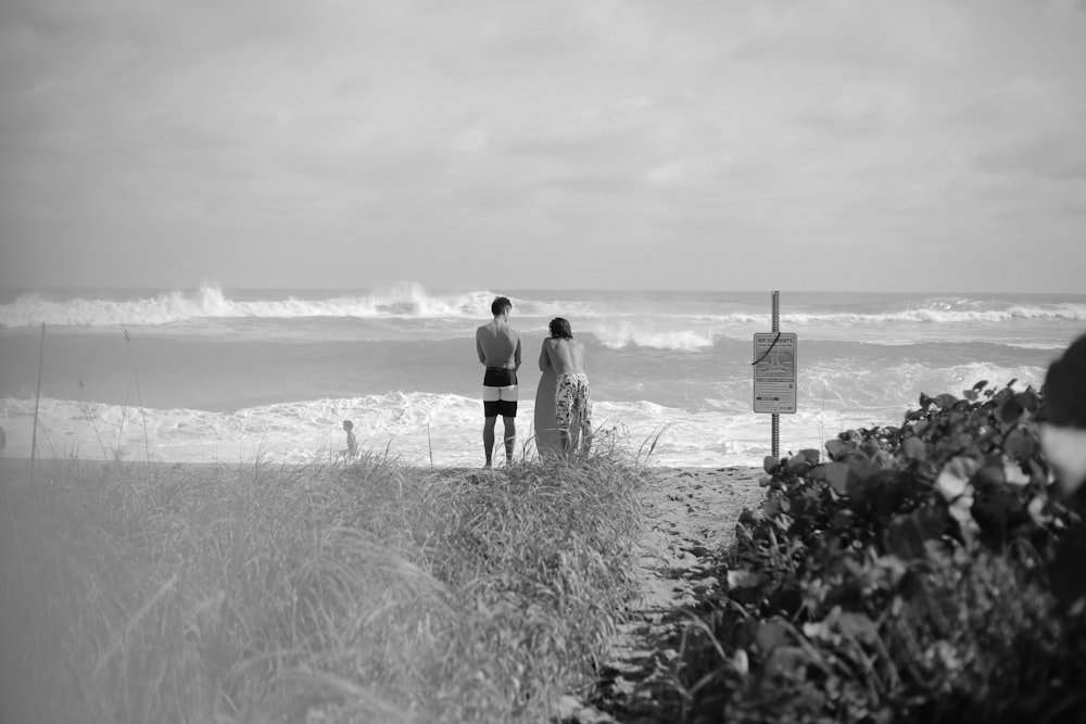 grayscale photo of couple walking on beach