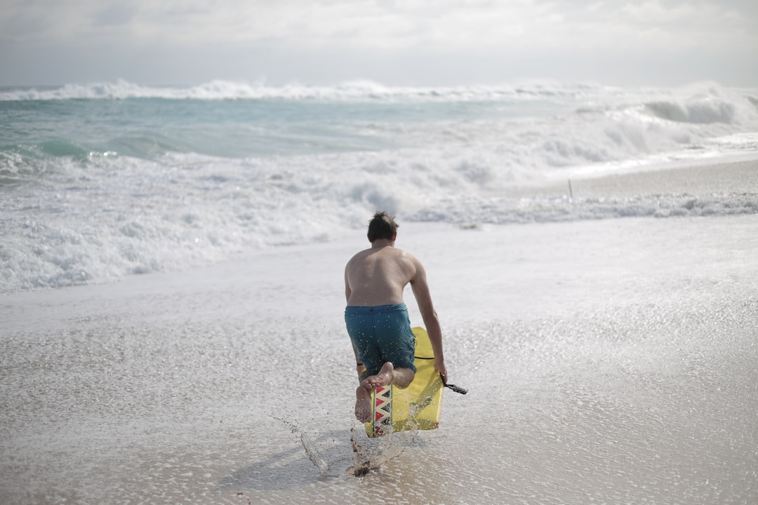 man in blue and yellow board shorts walking on beach during daytime