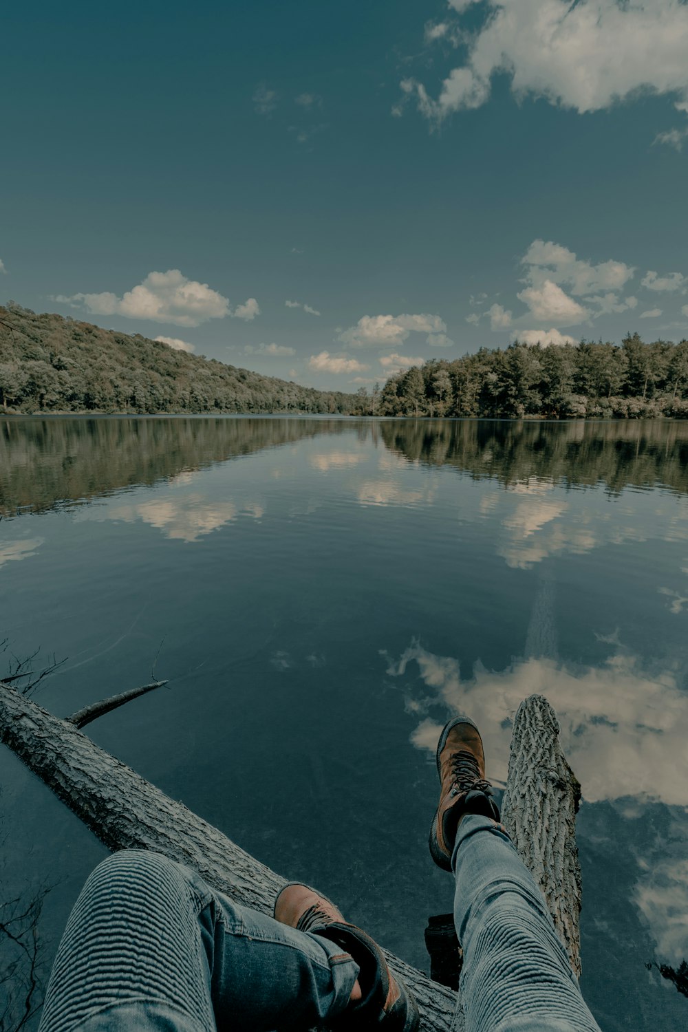 pessoa em tênis preto e branco sentada na doca de madeira sobre o rio durante o dia