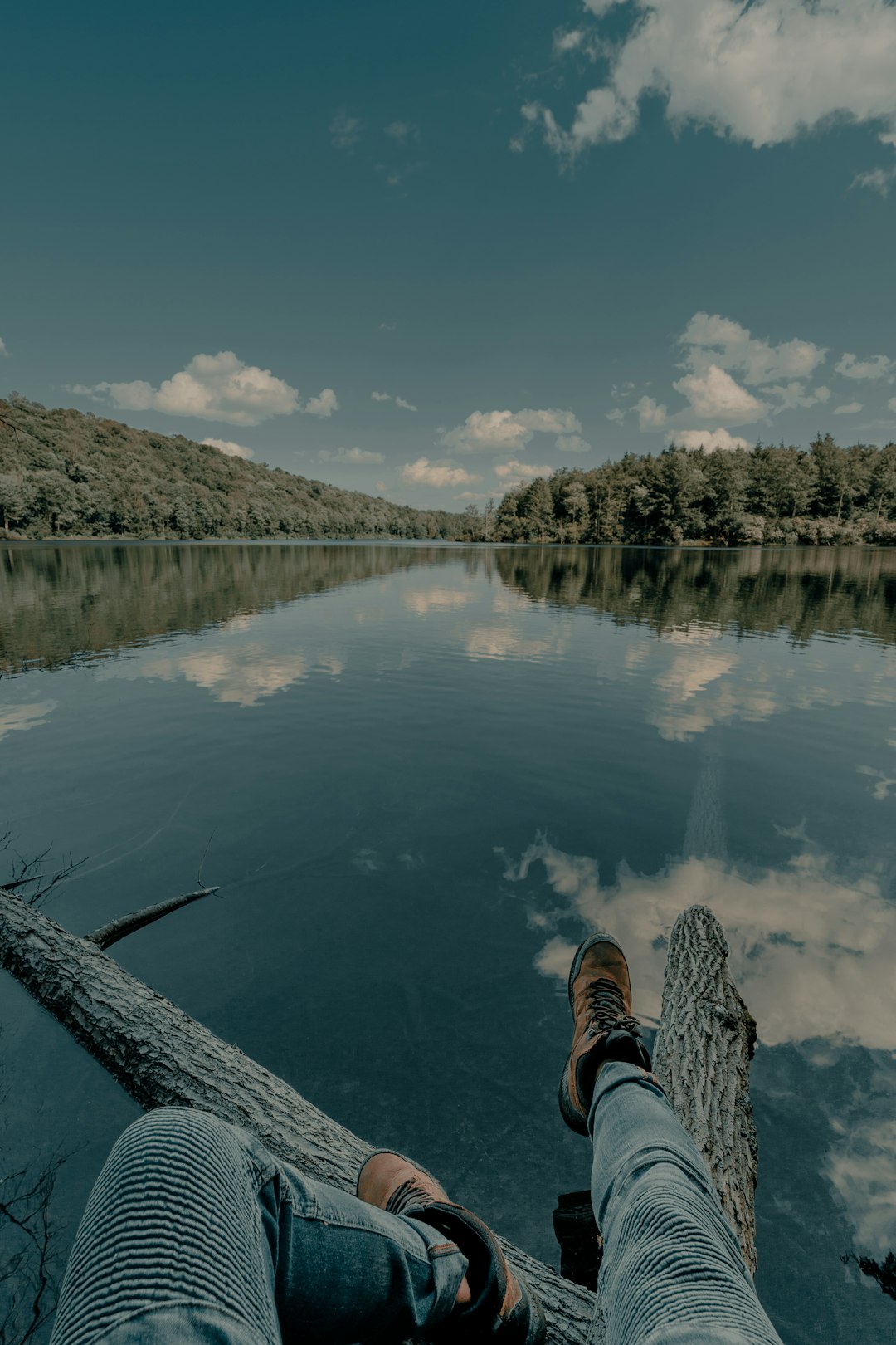 person in black and white sneakers sitting on wooden dock over the river during daytime