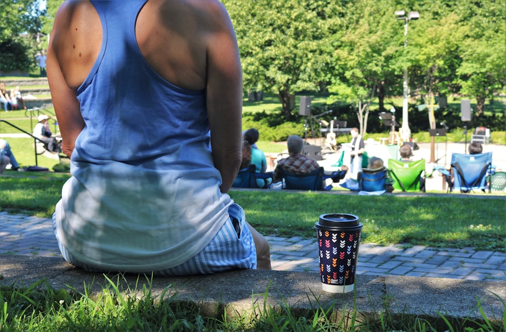 man in white tank top sitting on green grass field during daytime