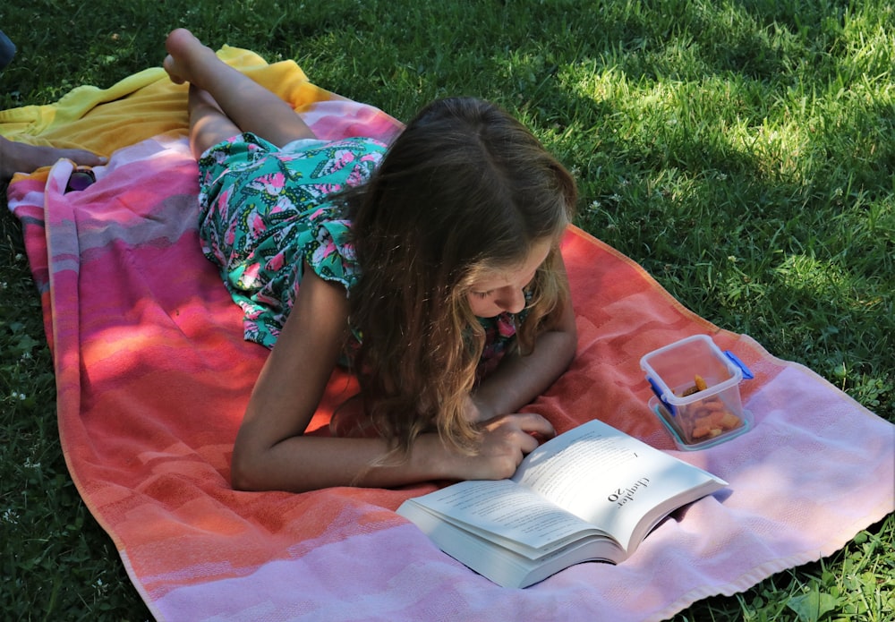 昼間、緑の芝生で本を読むピンクのドレスを着た女の子