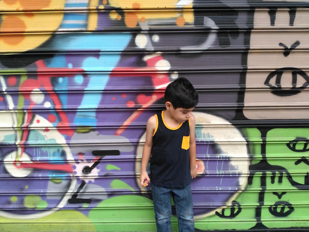 man in orange tank top and blue denim jeans standing beside wall