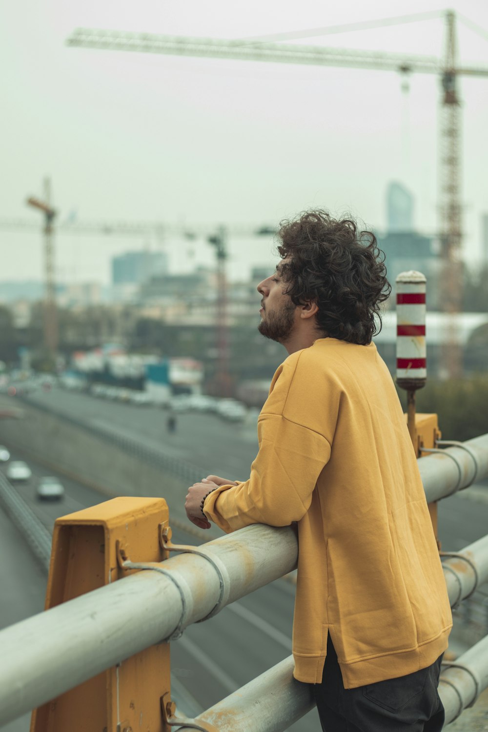 man in yellow long sleeve shirt standing on yellow metal railings during daytime