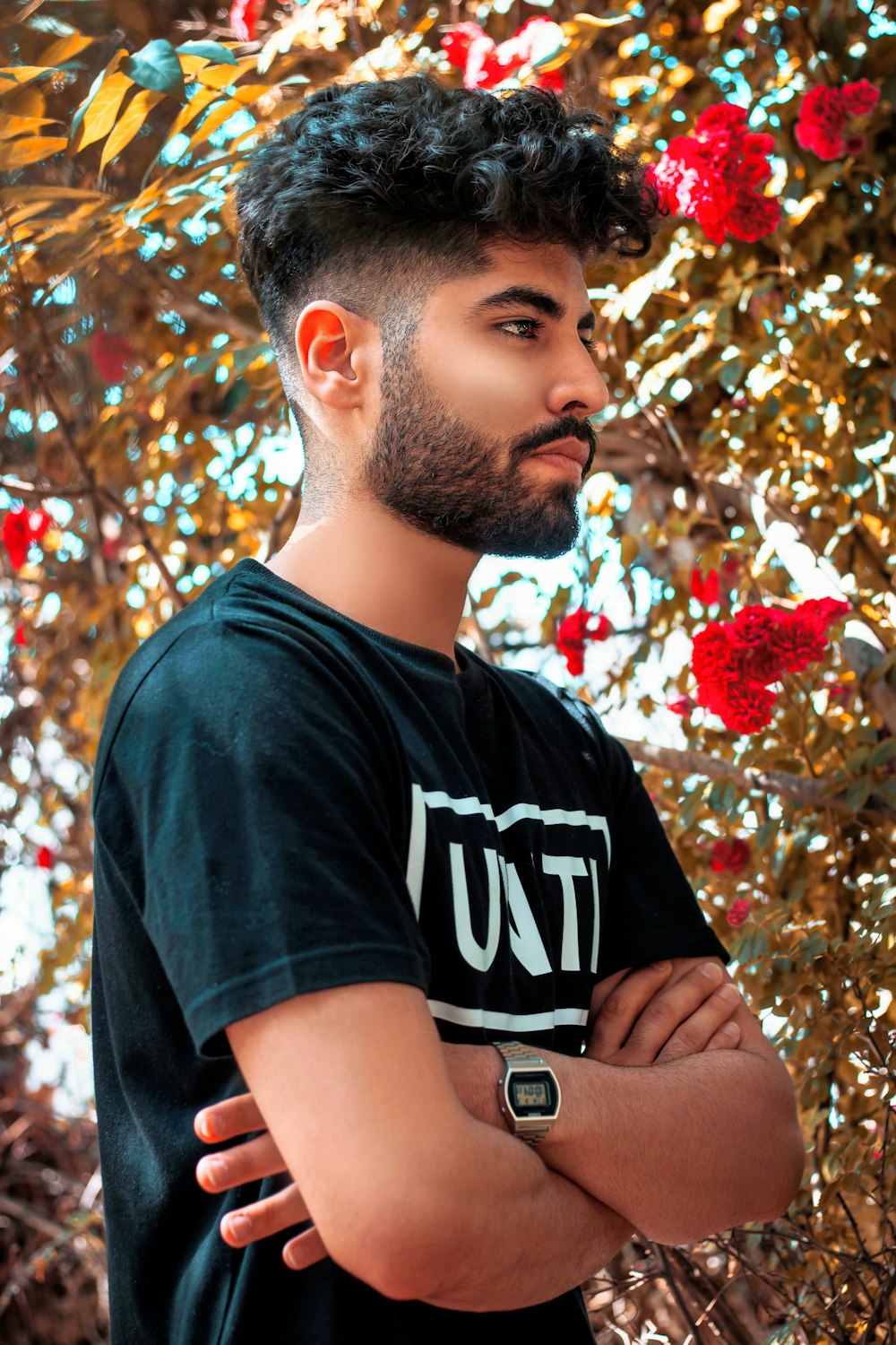 man in black crew neck t-shirt standing near red flowers