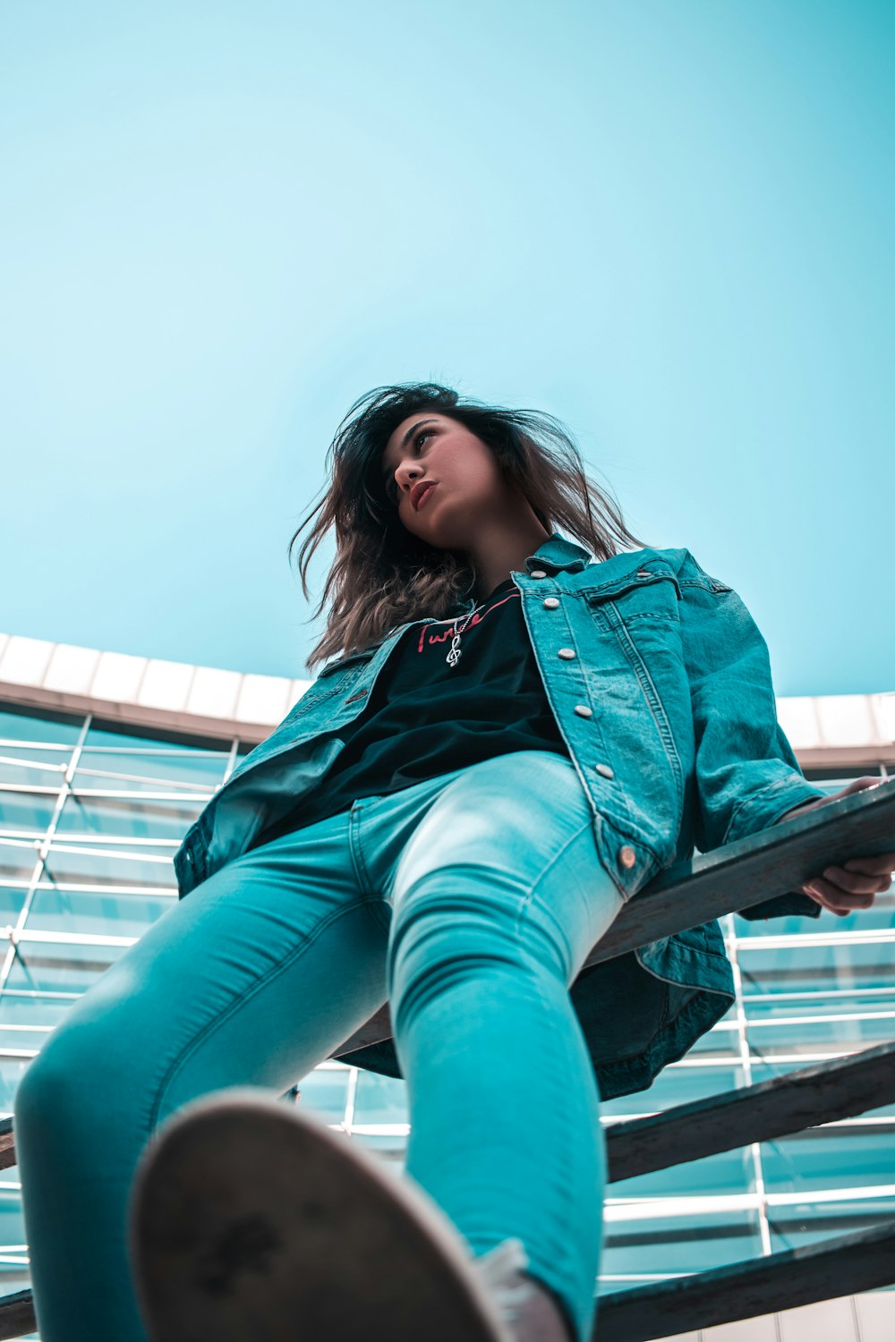 woman in blue denim jacket sitting on black metal railings during daytime