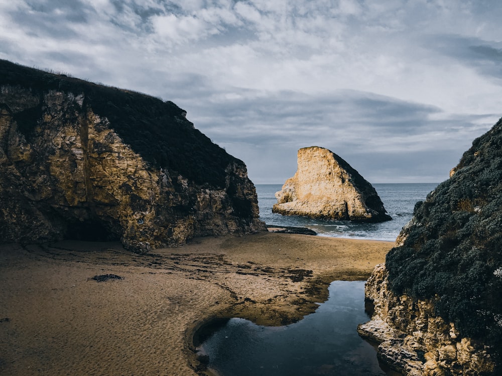 brown rock formation on sea shore under cloudy sky during daytime