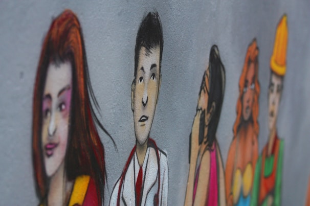 A mural on a wall depicts a series of stylized, colorful illustrations of diverse people in various poses. The characters are drawn with exaggerated features and are painted in a vibrant style. They appear to be lined up, each expressing different emotions or roles.