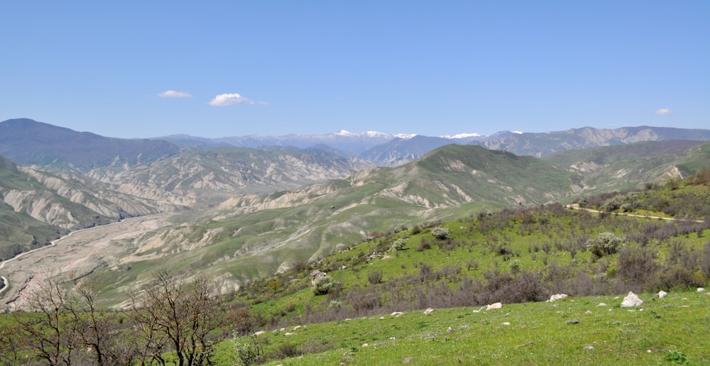 green grass field and mountains under blue sky during daytime