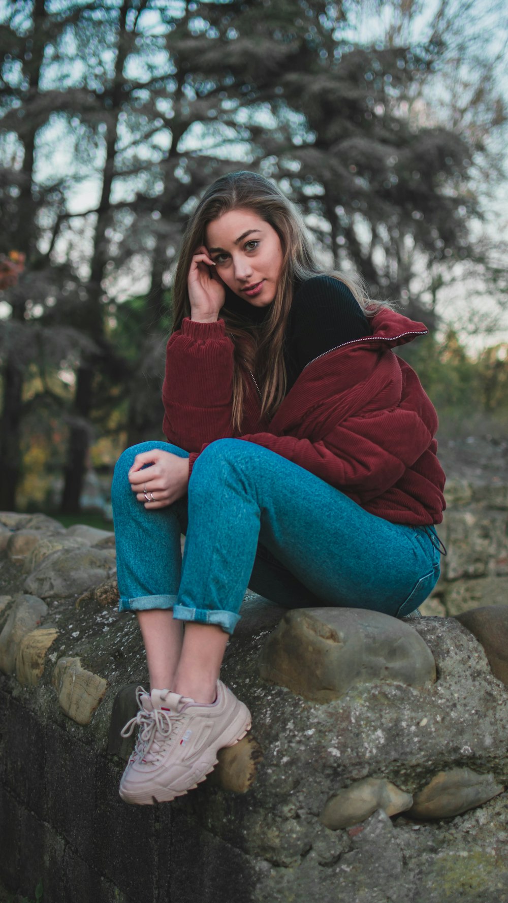 woman in red jacket and blue denim jeans sitting on rock