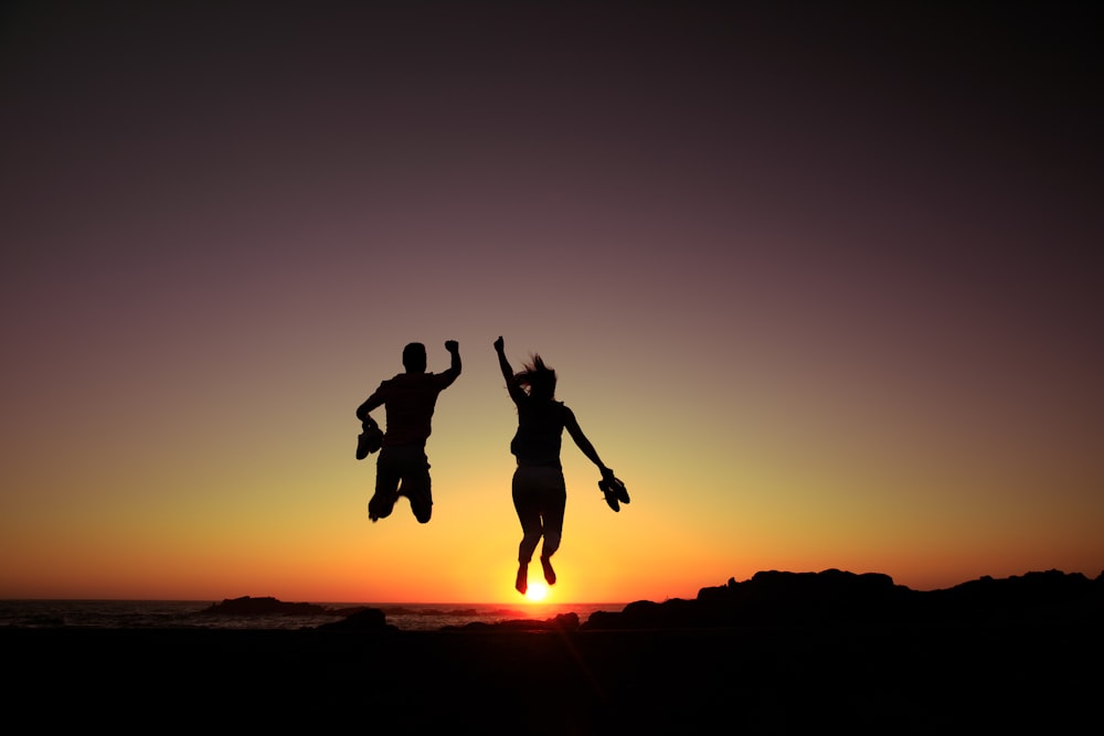 silhouette of 2 person jumping during sunset