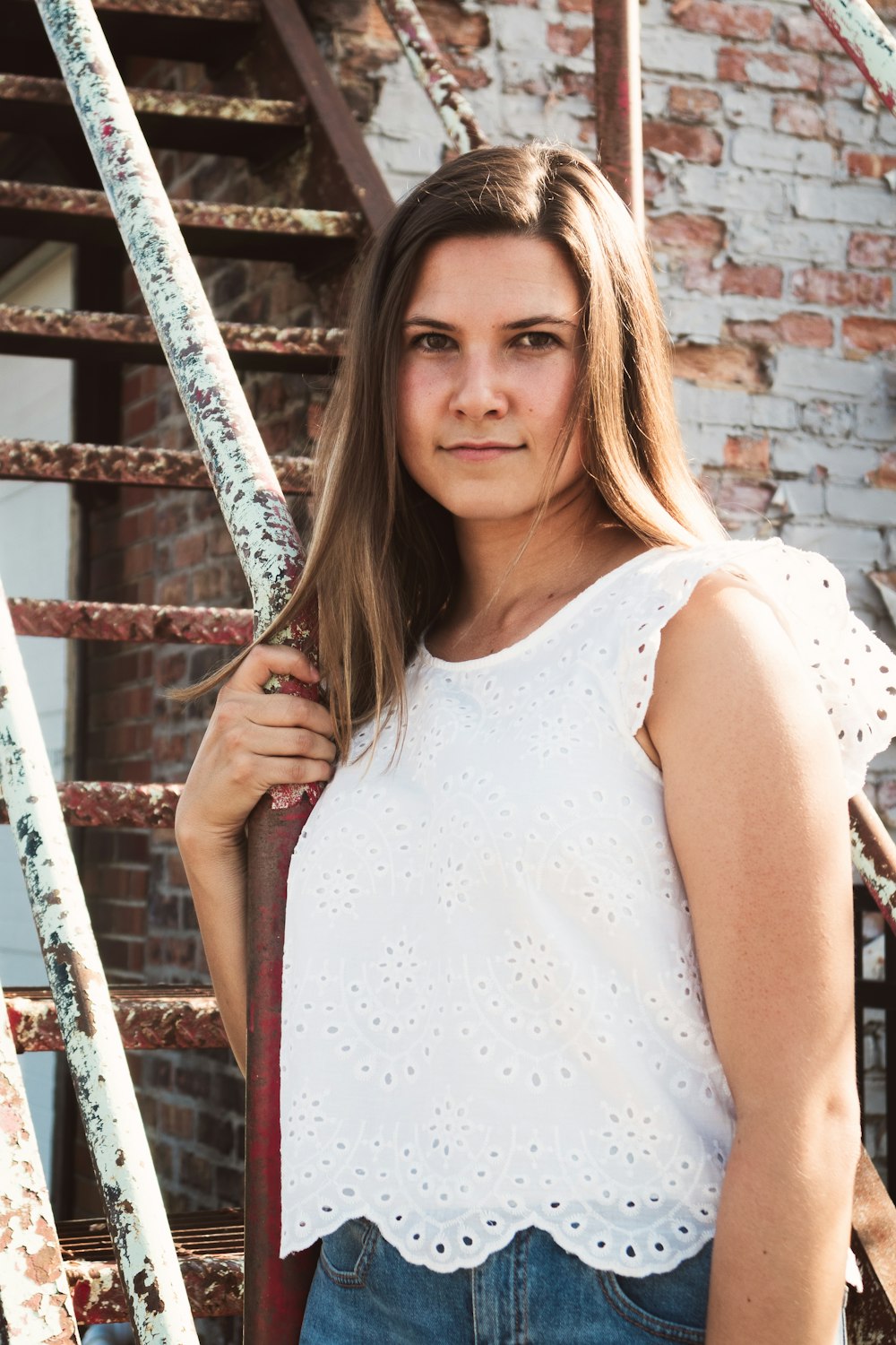 woman in white sleeveless dress holding on brown metal fence