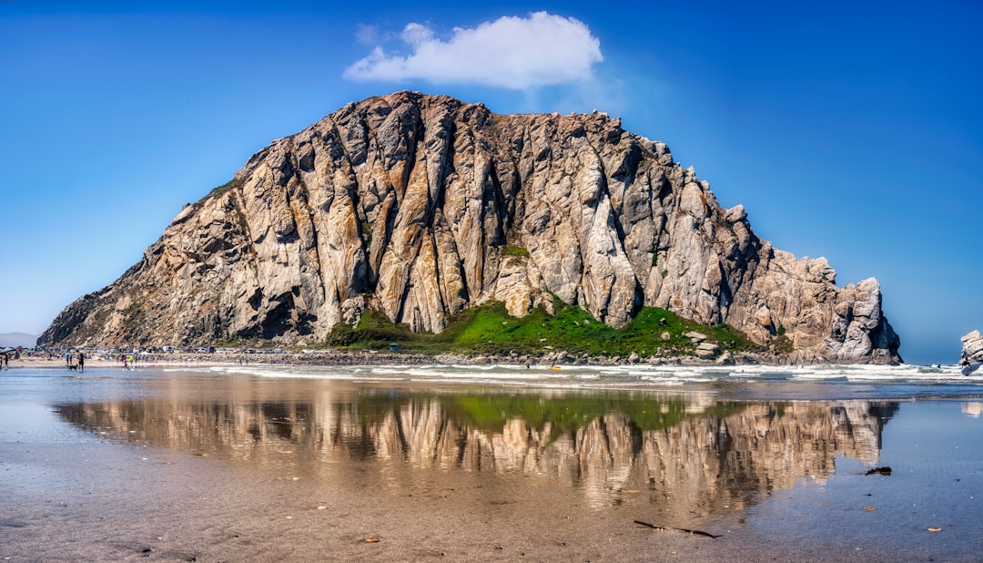 brown rocky mountain beside body of water under blue sky during daytime