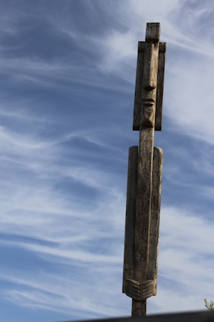 An atmospheric shot of a totem pole standing tall against a dramatic sunset sky, emphasizing silhouette and shadow.