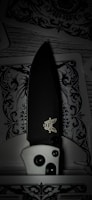 A detailed folding knife with a black blade and a logo visible near the handle rests on intricately designed playing cards, featuring decorative black and white patterns.