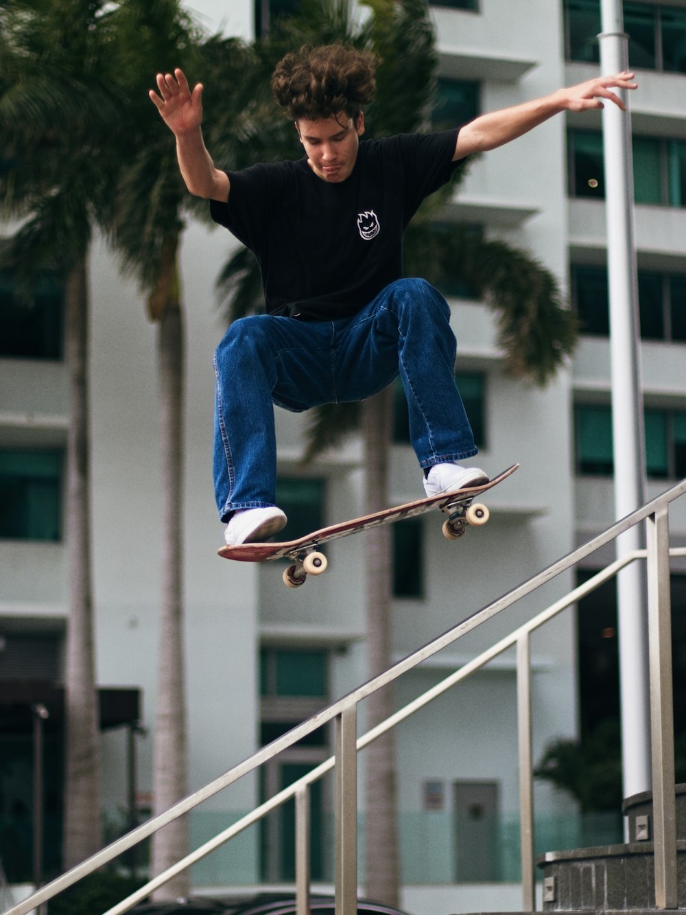 man in black t-shirt and blue denim jeans sitting on white metal railings during daytime