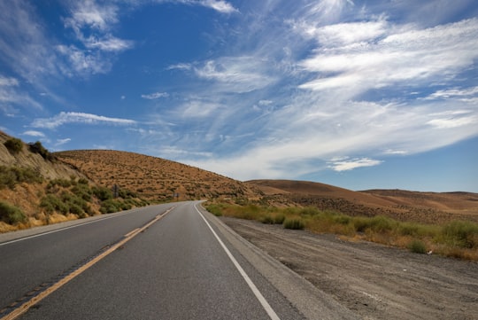 gray asphalt road between brown grass field under blue and white sunny cloudy sky during daytime in Arizona United States