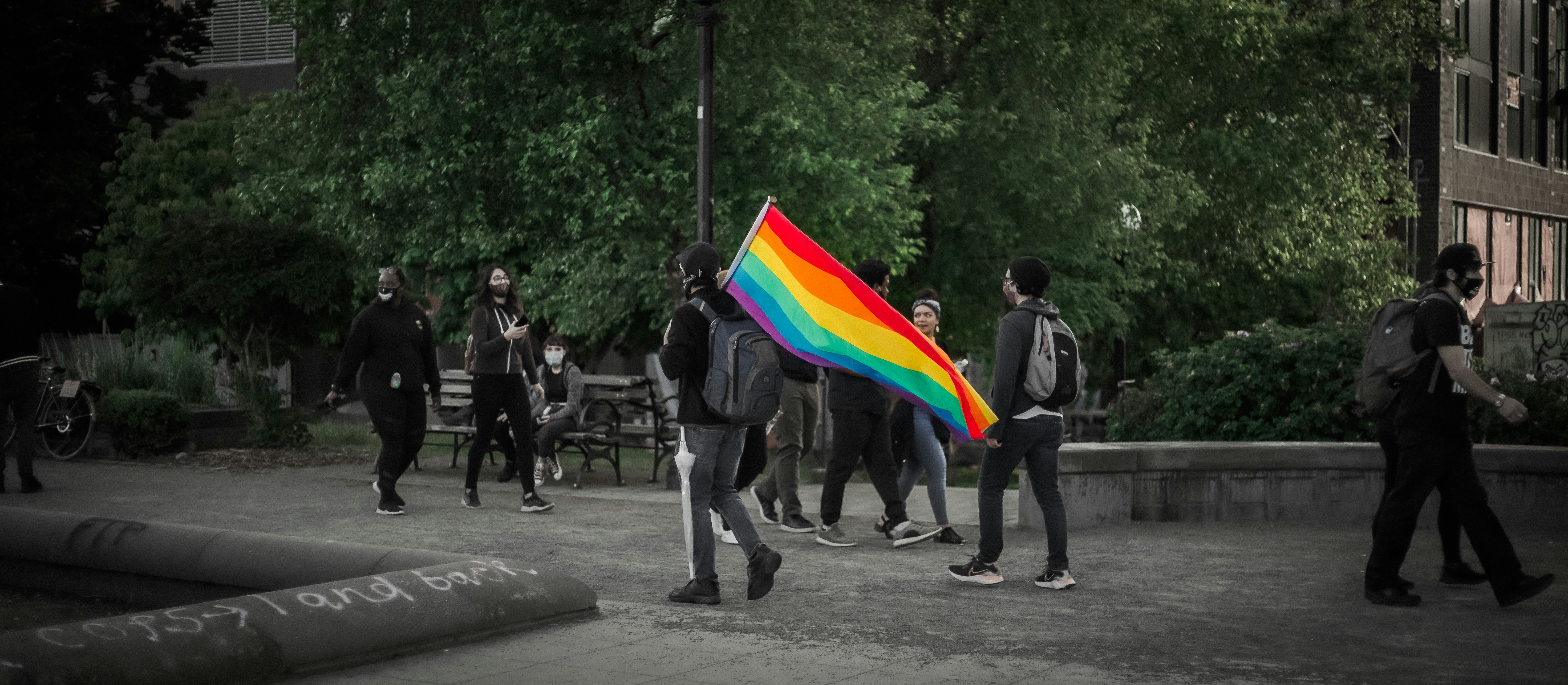 Man holding Pride flag walks through a park.
