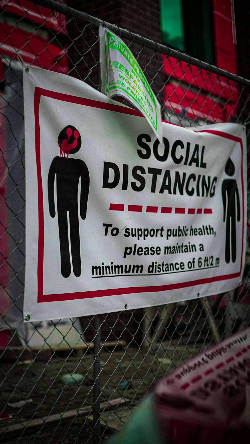 a social distancing sign on a chain link fence