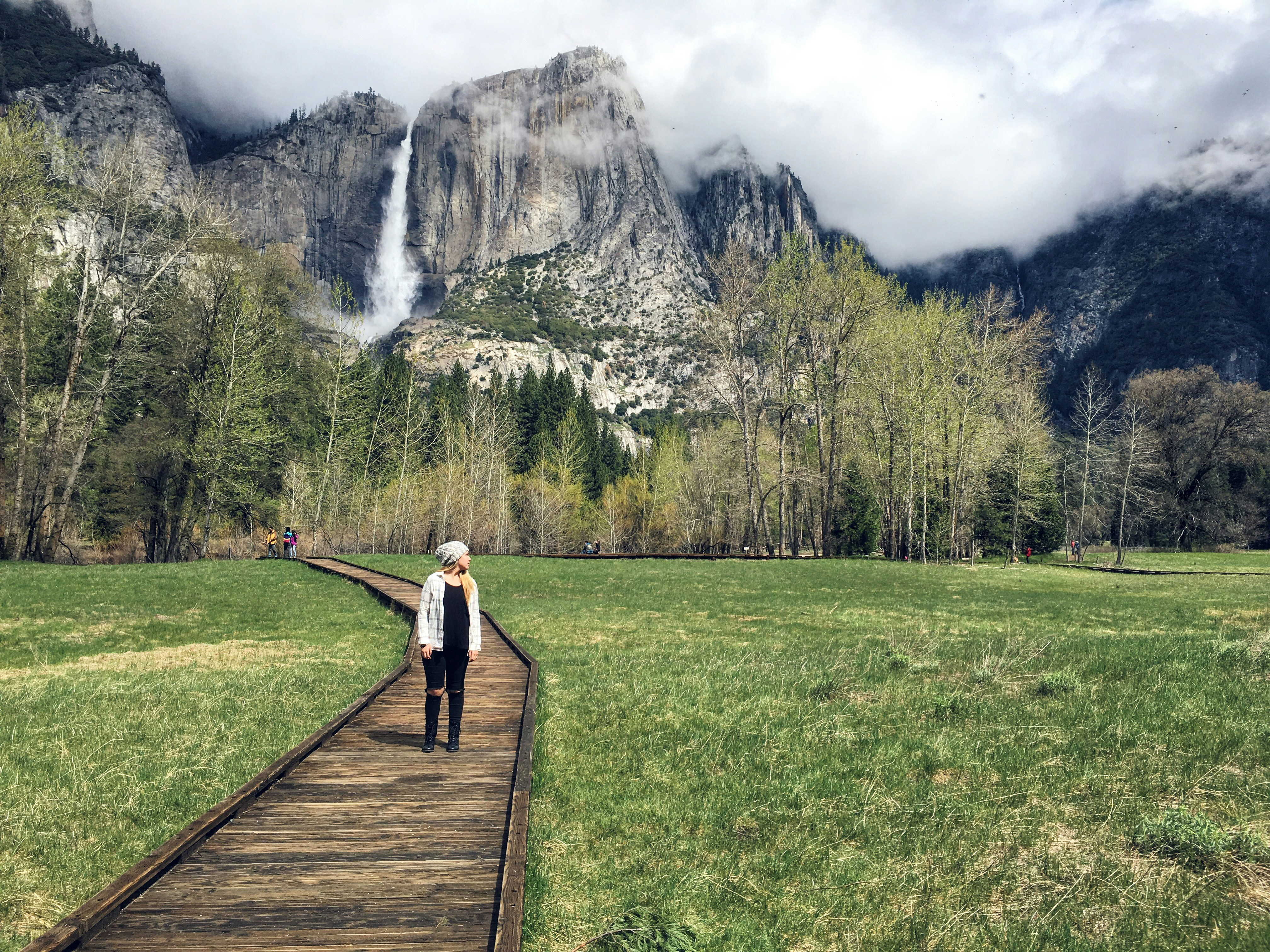 woman in white long sleeve shirt and black pants standing on brown wooden pathway during daytime, 