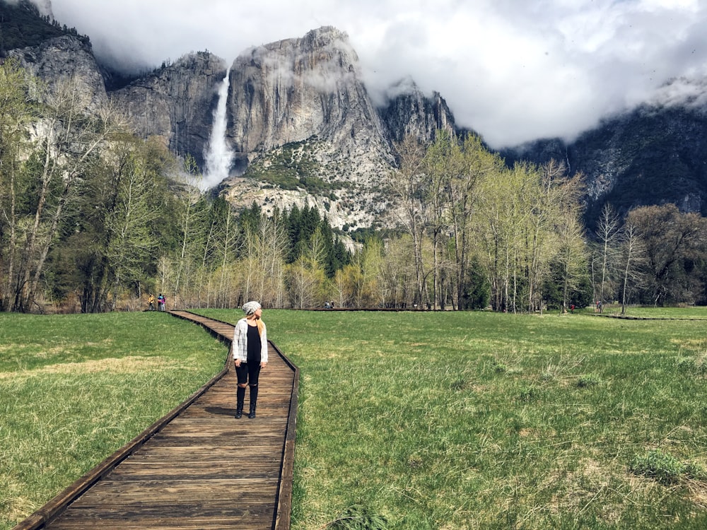 woman in white long sleeve shirt and black pants standing on brown wooden pathway during daytime