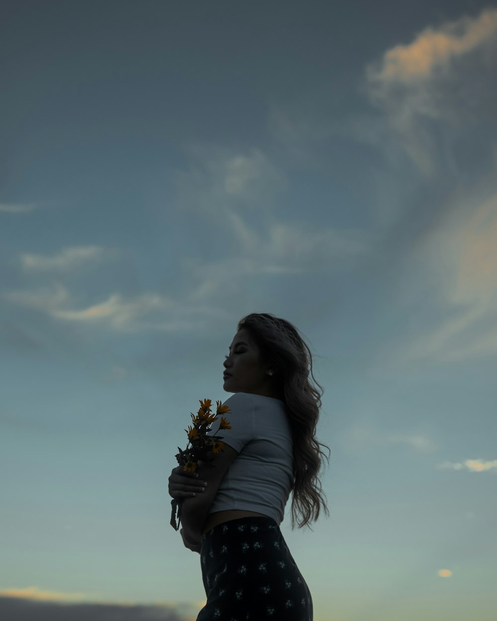 woman in black and white long sleeve shirt holding yellow flowers under white clouds and blue