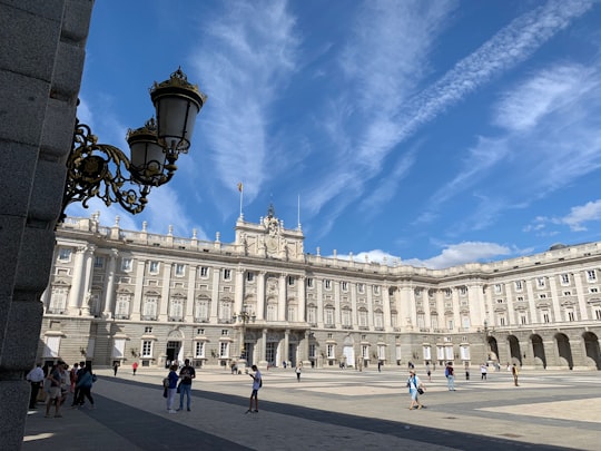people walking near white concrete building under blue sky during daytime in Royal Palace of Madrid Spain