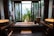 A modern bathroom features a large rectangular bathtub with a person relaxing inside. The room is decorated with sleek, dark wood elements and twin sinks on either side. Large windows offer a view of lush green plants outside, providing a sense of tranquility and connection with nature.