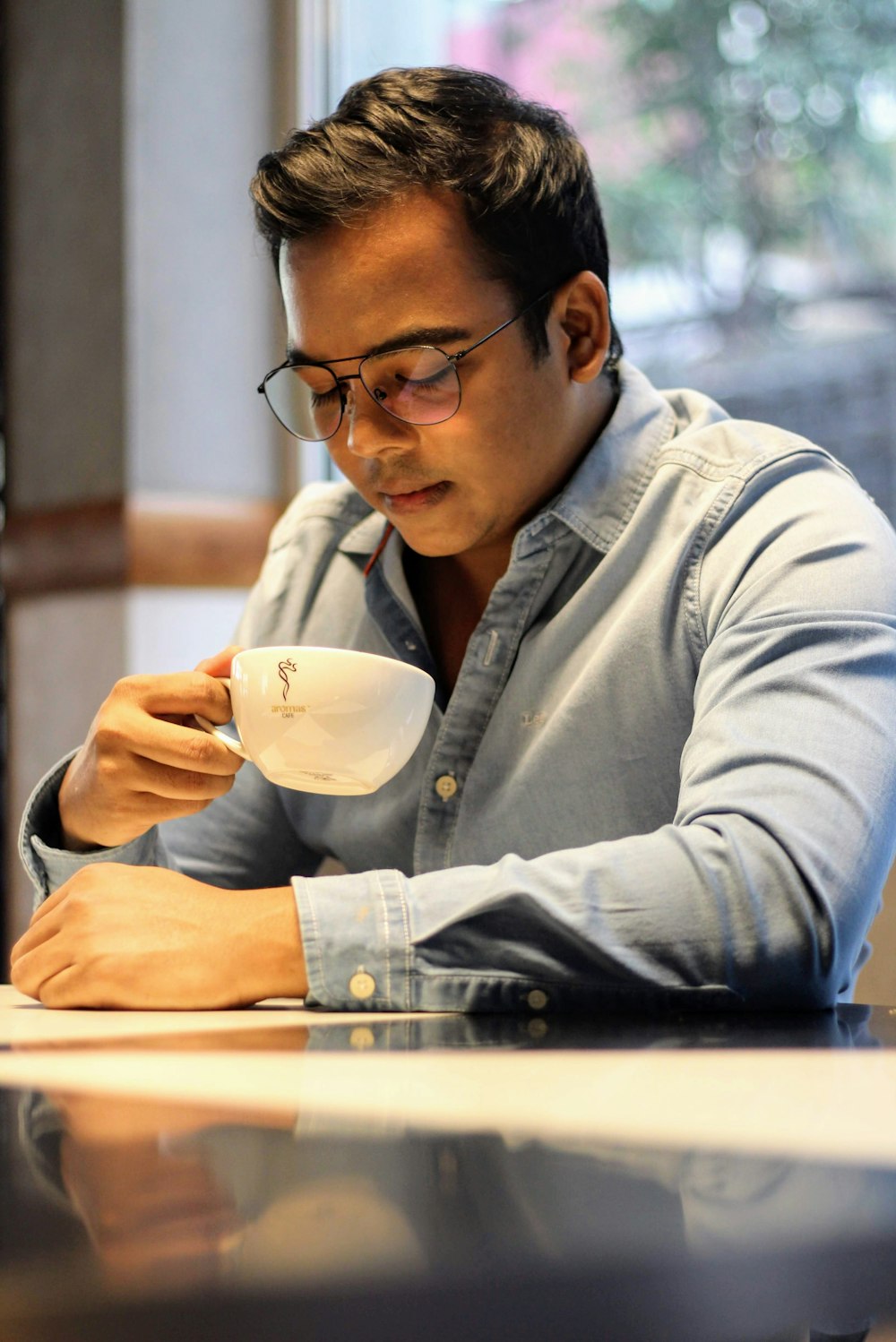 man in blue denim jacket holding white ceramic mug