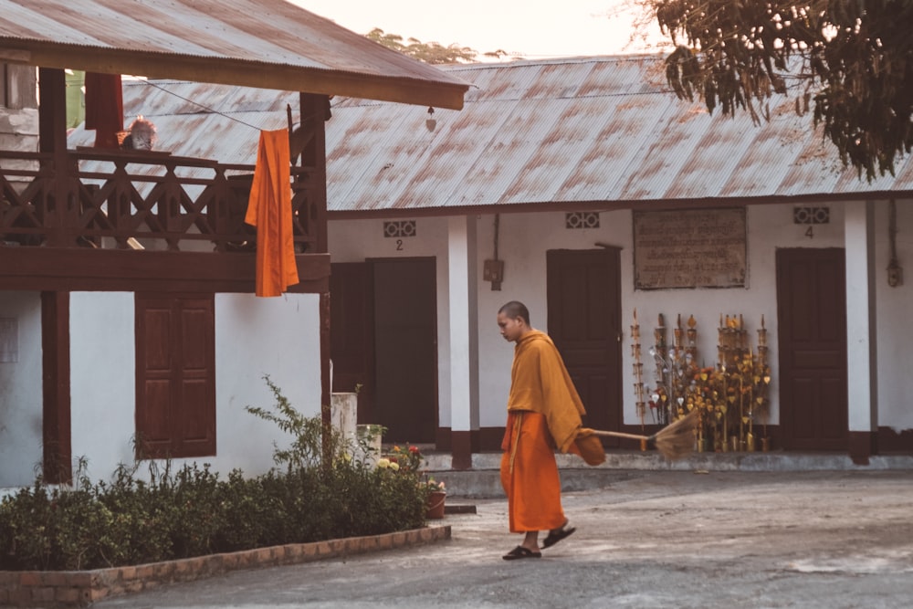 man in orange robe standing near white and brown building during daytime