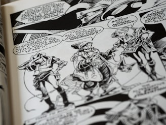 A black and white comic book page features three characters having a conversation. They wear futuristic attire with geometric patterns and accessories. Speech bubbles contain dialogue between the characters, and the background includes stylized designs.