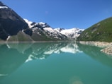 Snow-capped peaks of the Sawtooth Mountains with a clear turquoise alpine lake in the foreground.