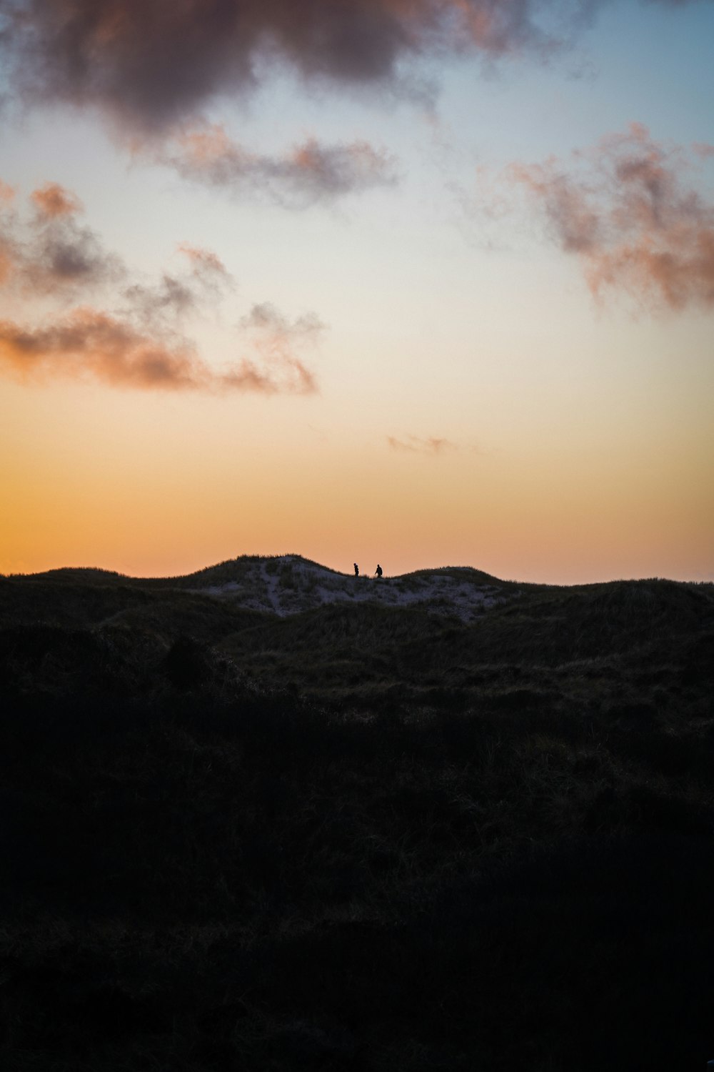 silhueta da pessoa em pé no topo da montanha durante o pôr do sol