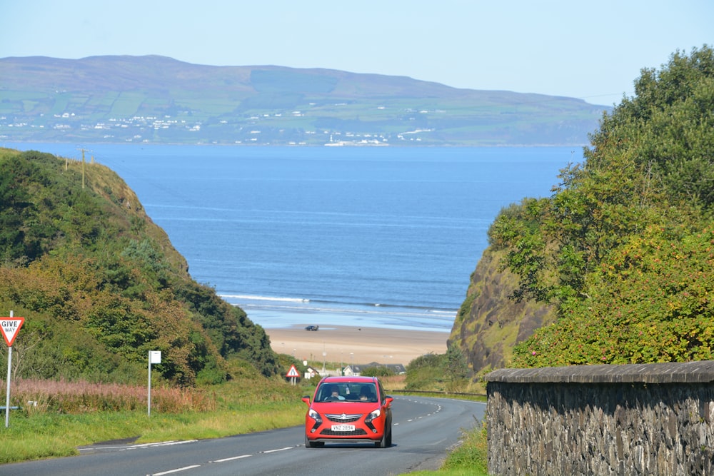 red car on road near body of water during daytime