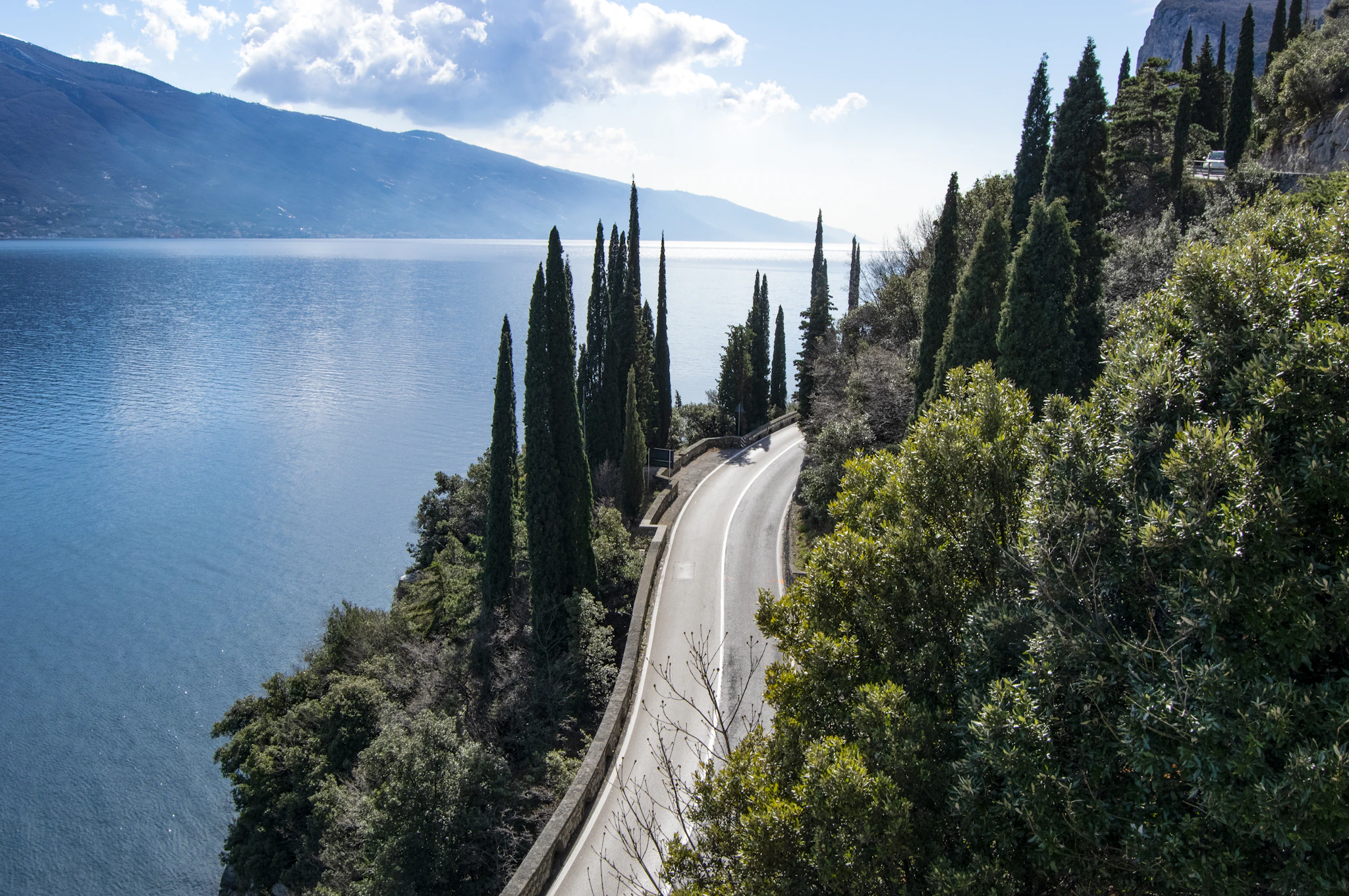 The road along Lake Garda between cypresses and the water, cycling Lake Garda